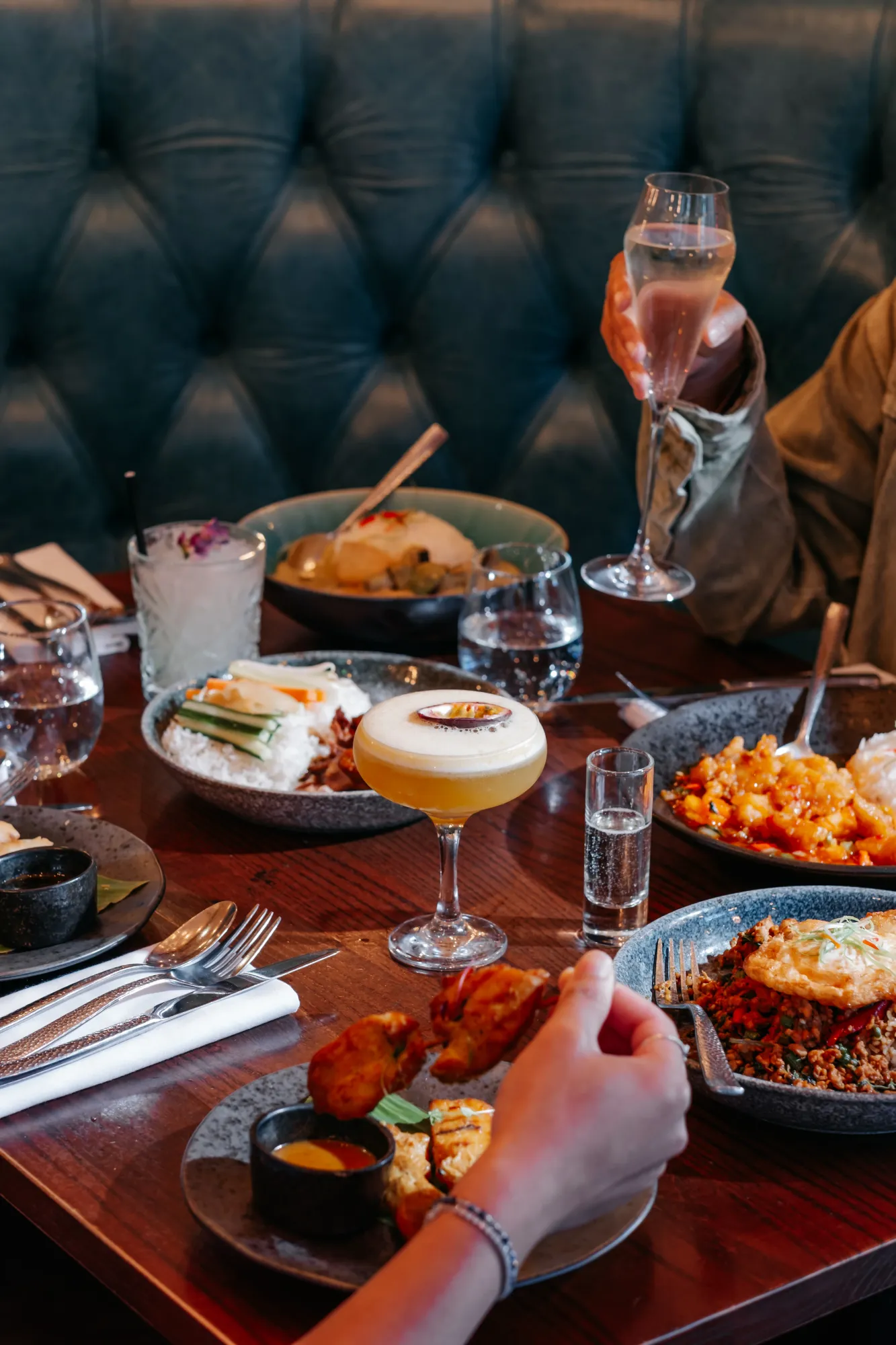 A group sharing Thai dishes and cocktails in a booth at Siamais